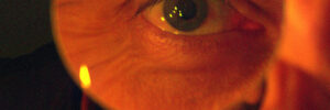 A person holds a magnifying glass up to their eye, enlarging their eye and eyebrow in the image.