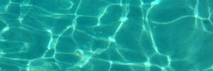 Sunlight reflects on the surface of clear blue water, creating a pattern of light and shadows.