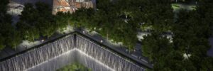 Aerial view of the 911 Memorial at night, featuring illuminated waterfalls and surrounding trees.
