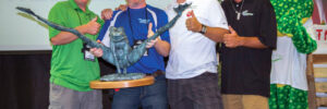 Four men pose with a large pondemonium award; a person in a frog costume smiles in the background.