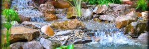 A landscaped garden pond by a koi pond contractor, with rocks, waterfalls, lush plants, and water lilies.