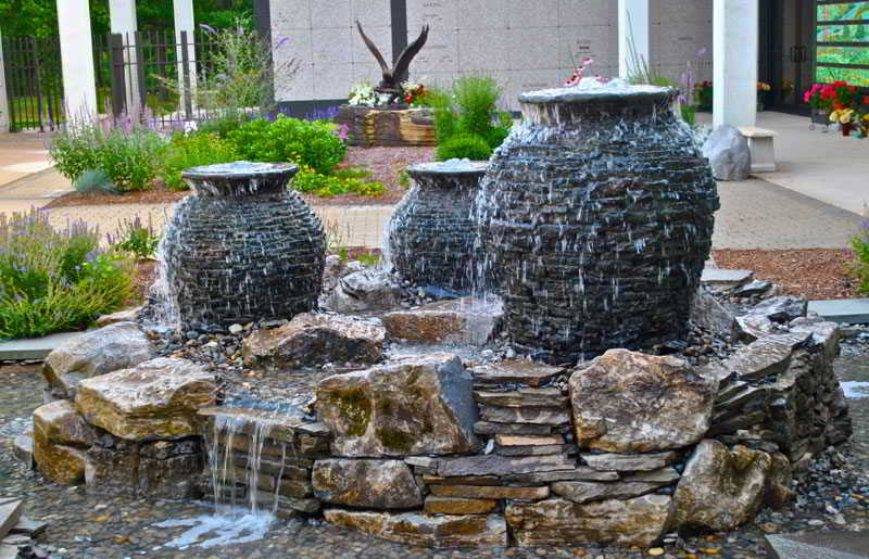 Three stone urn fountains with water cascading over rocks in an outdoor garden setting.