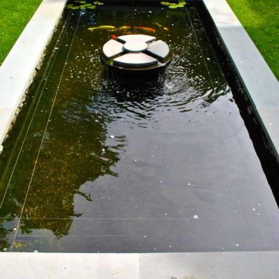 Rectangular reflecting pool with circular stone fountain in the center, surrounded by grass, with a bench at one end.