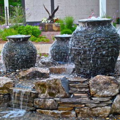 Three stone urn fountains with water cascading over rocks in an outdoor garden setting.