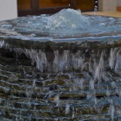 Water flows over the edge of a tiered stone fountain with water bubbling at the top.