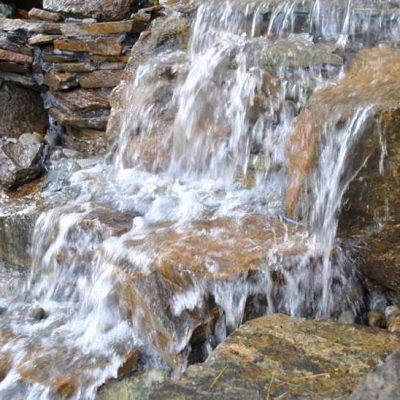 Water flows over rocks in a small man-made waterfall, with stone slabs stacked on the left side.