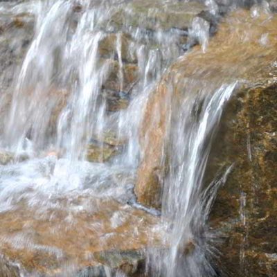 Water cascades over a series of natural stone steps, creating a small, multi-level waterfall.