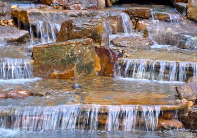 Small waterfalls cascade over layered rocks in a natural outdoor setting.