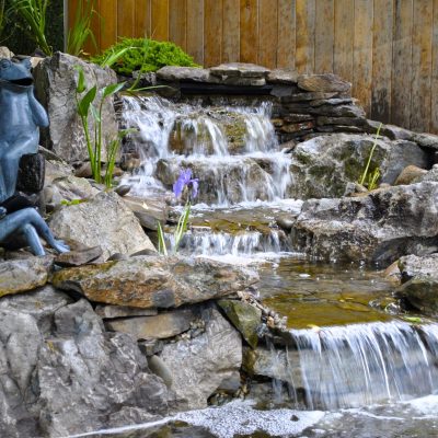 A small stone waterfall garden with two frog sculptures sitting on rocks beside the flowing water.
