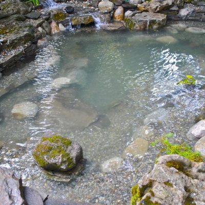 Small artificial pond with clear water, surrounded by rocks and pebbles, with a small waterfall in the background.