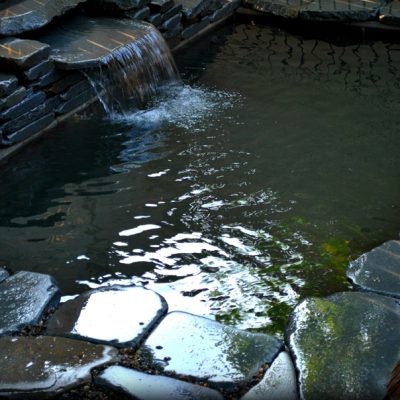 A small artificial pond with a stone border and a short waterfall flowing into the water.