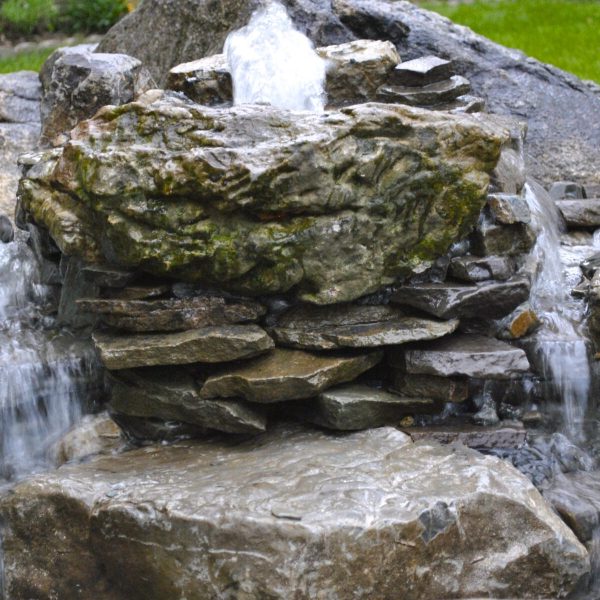 Small backyard rock fountain with water flowing over stacked stones and green grass in the background.