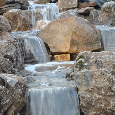 Water flows over multiple tiers of rocks in a small, artificial waterfall and pond feature.