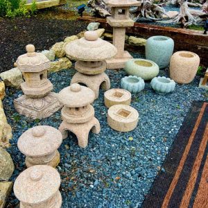 A display of stone lanterns, pots, and ornaments arranged on gravel in an outdoor garden center.