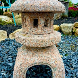 Stone Japanese lantern with a rounded top and cut-out windows, standing on gravel in a garden setting.