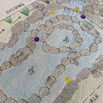 Hand-drawn pond design on graph paper with labeled zones, rocks, water flow directions, and identified caves.